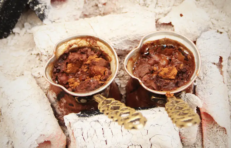 Two copper cezves foaming with Turkish coffee, nestled in hot sand beneath glowing charcoal