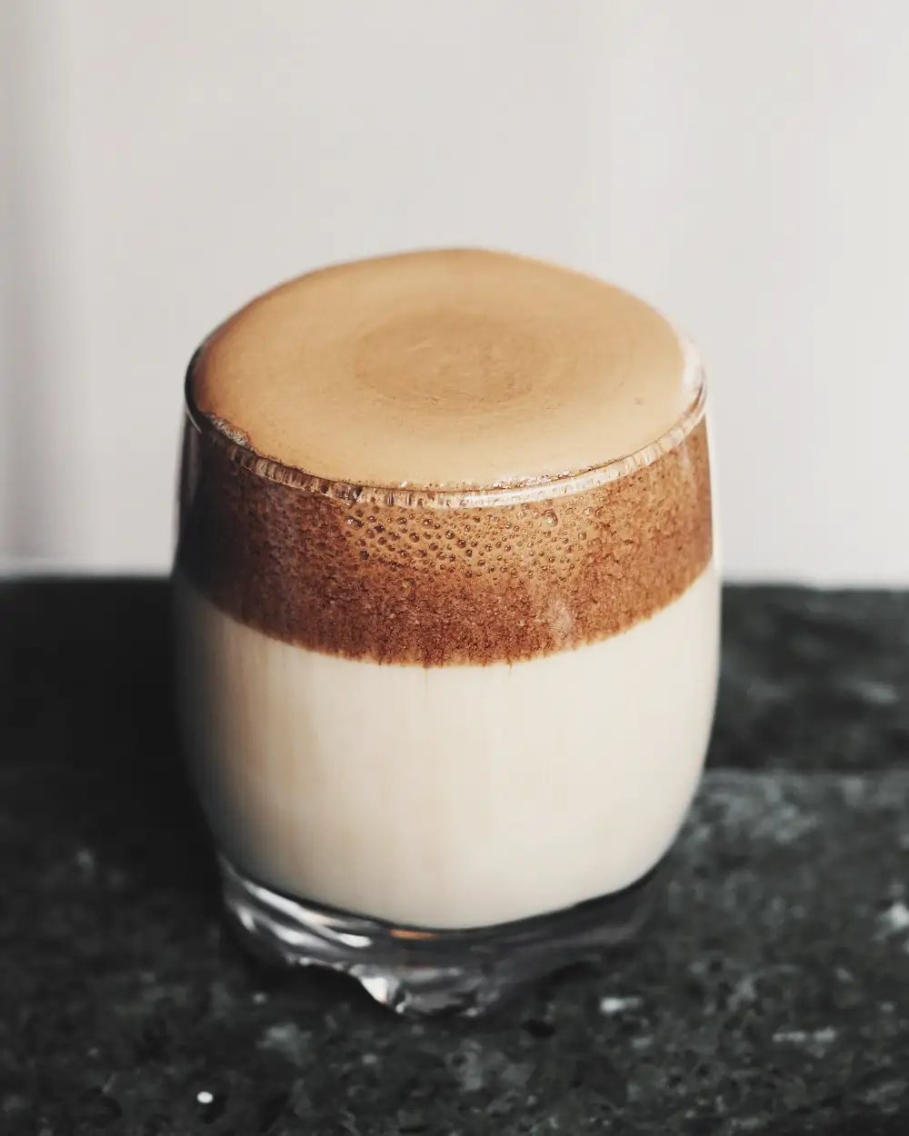 Whipped coffee layered over milk in a tall glass